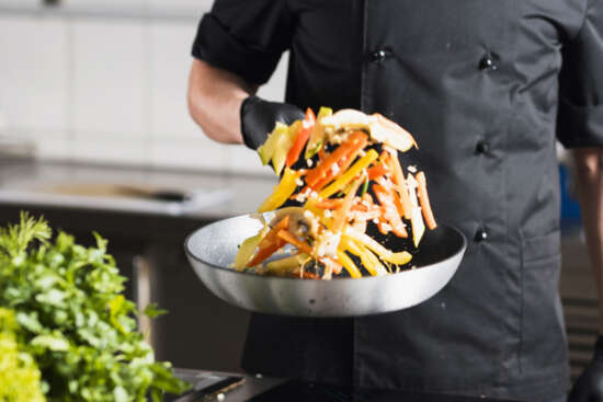 Curs Manipulacio Aliments online Ecotècnic. Persona cuinant verdures amb guants, seltejant a la paella